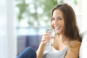 mujer sentada en un sofá mirando a la cámara con un vaso de agua